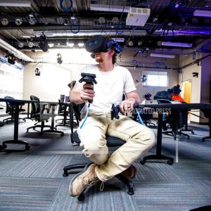 In this Wednesday, June 9, 2021, photo, City of Gillette worker CJ Ellis looks around inside of a piece of work equipment from the comfort of a Gillette College classroom while participating in a safety exercise done in virtual reality in Gillette, Wyo. VR goggles protruded from their faces but inside their minds, they experienced what it's like to stand in a coal mine from the seat of a classroom chair, the Gilette News Record reports. The blind spot training program that Gillette College Mine Safety and Health Administration Instructor Nick Ullrich walked the city workers through recently is the first of what he hopes becomes many training and teaching programs that can use the college's new VR classroom. (Mike Moore/Gillette News Record via AP)