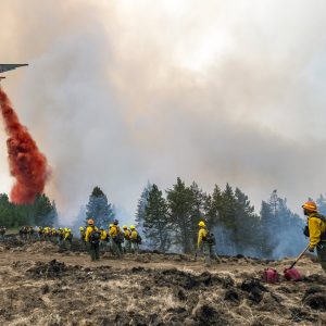 Wildland firefighters watch and take video with their cellphones as a plane drops fire retardant on Harlow Ridge above the Lick Creek Fire, southwest of Asotin, Wash., Monday, July 12, 2021. The fire, which started last Wednesday, has now burned over 50,000 acres of land between Asotin County and Garfield County in southeast Washington state. (Pete Caster/Lewiston Tribune via AP)