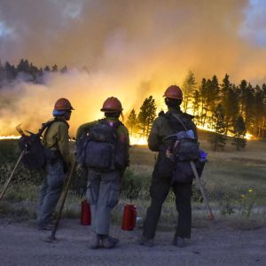 Firefighters watch a hillside burn on the Northern Cheyenne Indian Reservation, Wednesday, Aug 11, 2021, near Lame Deer, Mont. The Richard Spring fire was threatening hundreds of homes as it burned across the reservation. (AP Photo/Matthew Brown)