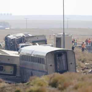 FILE - In this Sept. 27, 2021, file photo, workers stand near train tracks next to overturned cars from an Amtrak train that derailed near Joplin, Mont. A derailment of an Amtrak train in Montana that killed three people in 2021 was caused by a railroad track that was bent along a curve near the accident site, federal investigators said Thursday, July 27, 2023 in a final report. (AP Photo/Ted S. Warren, File)