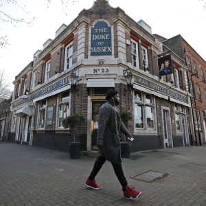 A man walks past the Duke of Sussex pub with a sign depicting the image of Britain's Prince Harry and his wife Meghan, near Waterloo station, London, Tuesday March 9, 2021. Prince Harry and Meghan's explosive TV interview has divided people around the world, rocking an institution that is struggling to modernize with claims of racism and callousness toward a woman struggling with suicidal thoughts. (AP Photo/Frank Augstein)